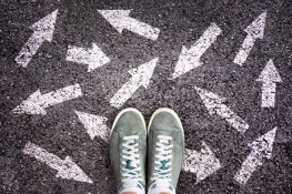 Sneaker shoes and arrows pointing in different directions on asphalt ground. career path choice concept